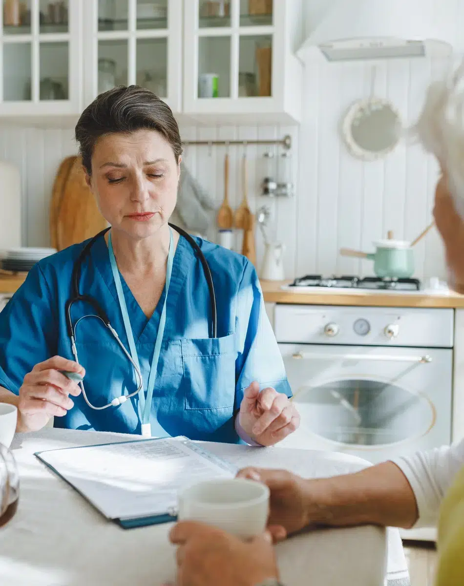 Infirmière discutant avec une personne âgée dans une cuisine.