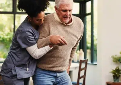 Infirmière soutenant un homme âgé dans une maison lumineuse.