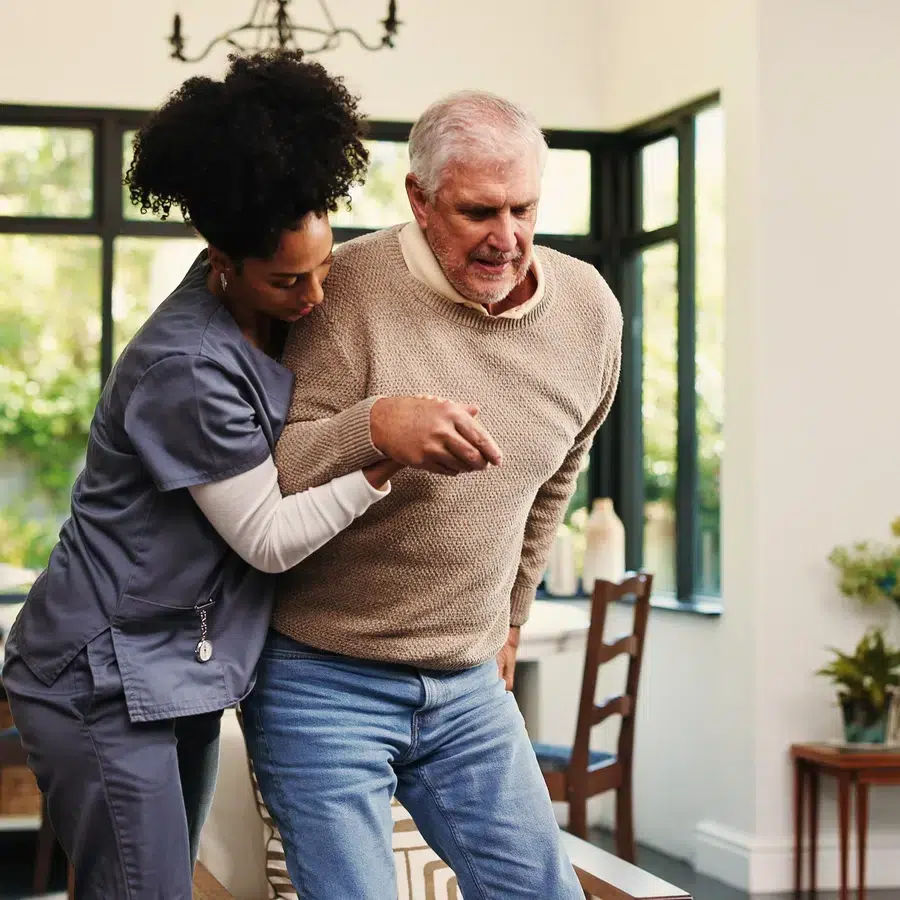 Infirmière soutenant un homme âgé dans une maison lumineuse.