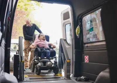 Homme aidant une personne en fauteuil roulant à monter dans un véhicule.