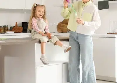 Femme et enfant jouant avec des bulles dans une cuisine moderne.