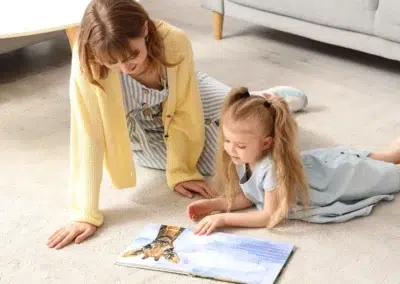 Femme et enfant lisant un livre ensemble sur le sol.