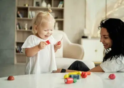 Enfant jouant avec des jouets colorés, femme souriante.